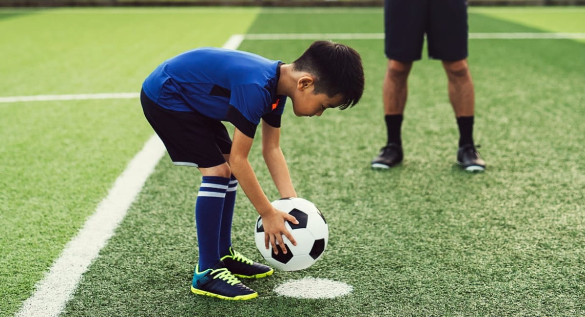 Young boy practising penalty kick as dad watches