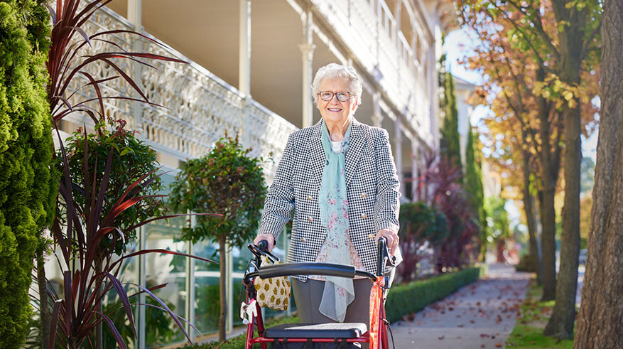 Aged care resident smiling and walking with a walker