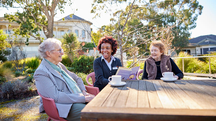 Residents and staff laughing and enjoying a conversation outside on an Autumn day