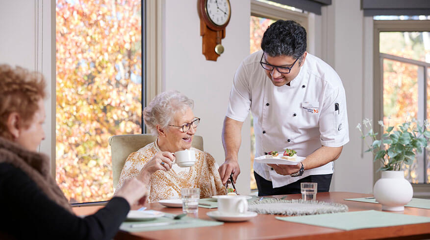 Residents smiling and receiving lunch from the chef