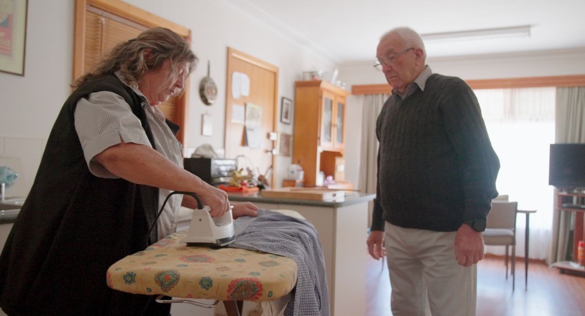 A home care worker ironing with her customer watching