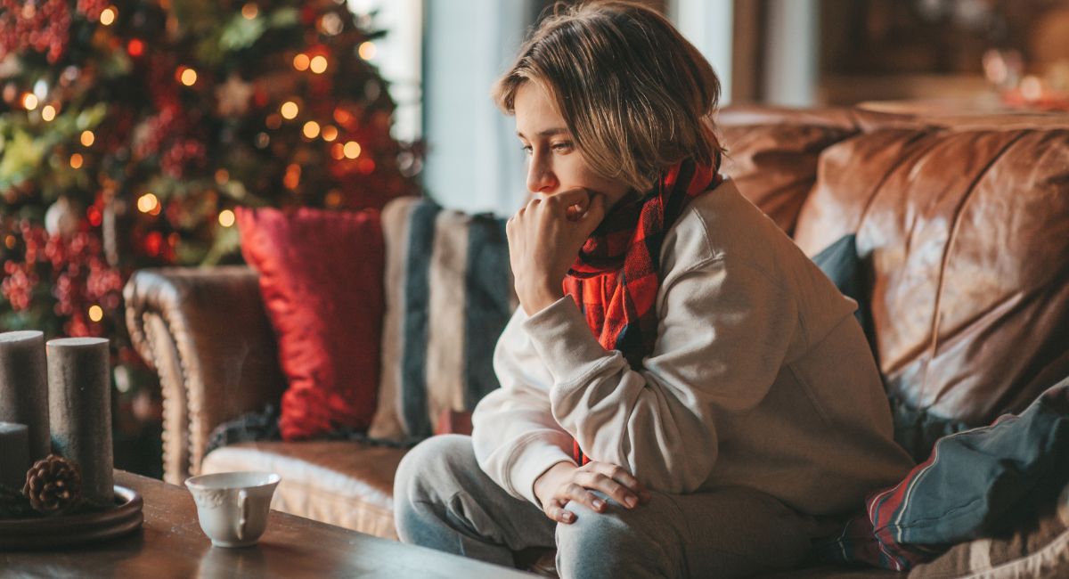 A young depressed woman sitting alone in front of a Christmas tree