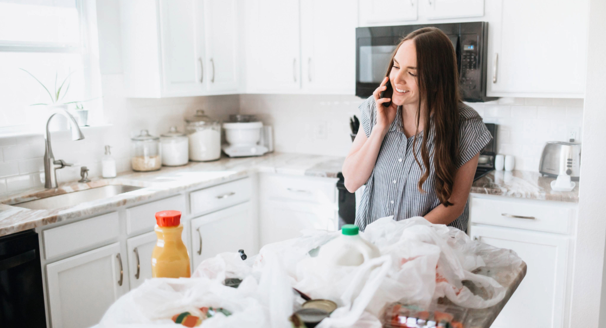 A woman on the phone while standing over a table of groceries