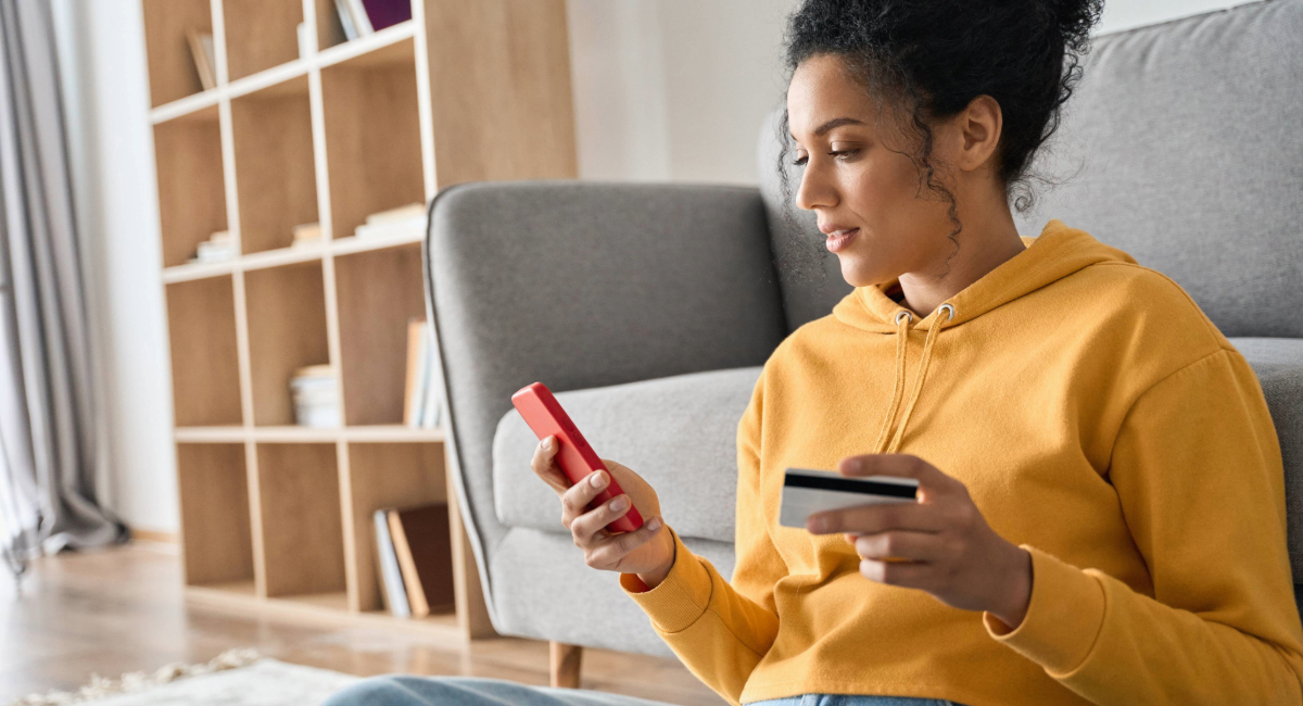 A young woman looking at her phone holding a bank card in her hand