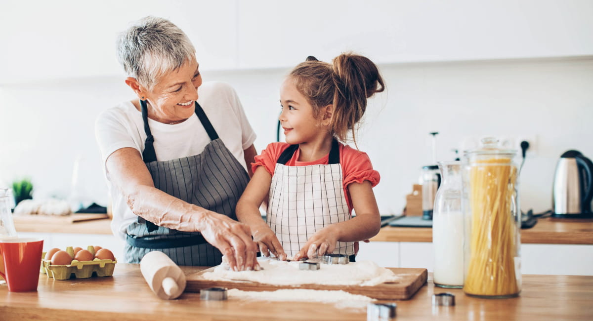 An older woman cooking in the kitchen with her young granddaughter