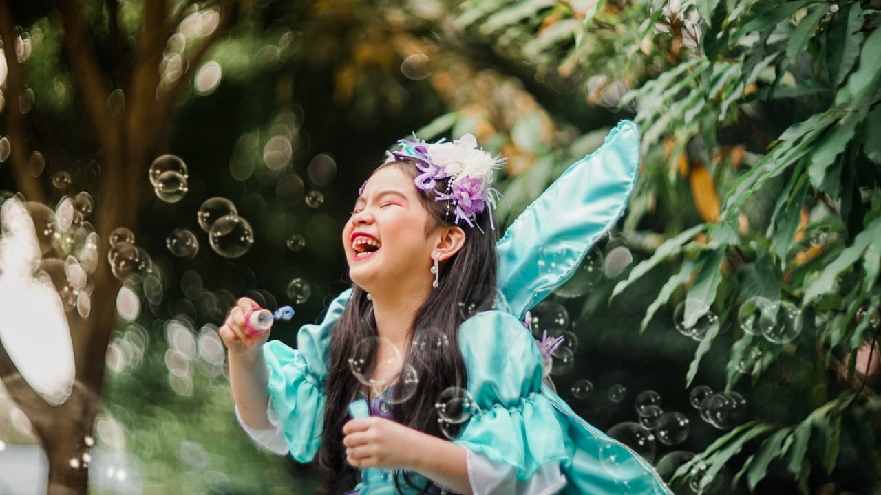 Young girl in fairy costume laughing and blowing bubbles