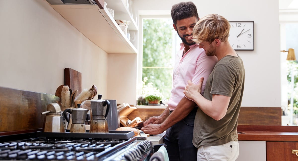 Two men laughing as they cook breakfast